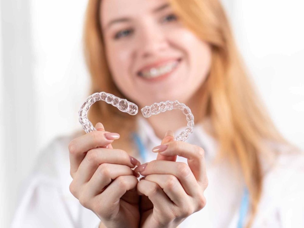 cuidado-dental-nina-sonriente-con-cabello-rojo-sosteniendo-alineadores-en-forma-de-corazon